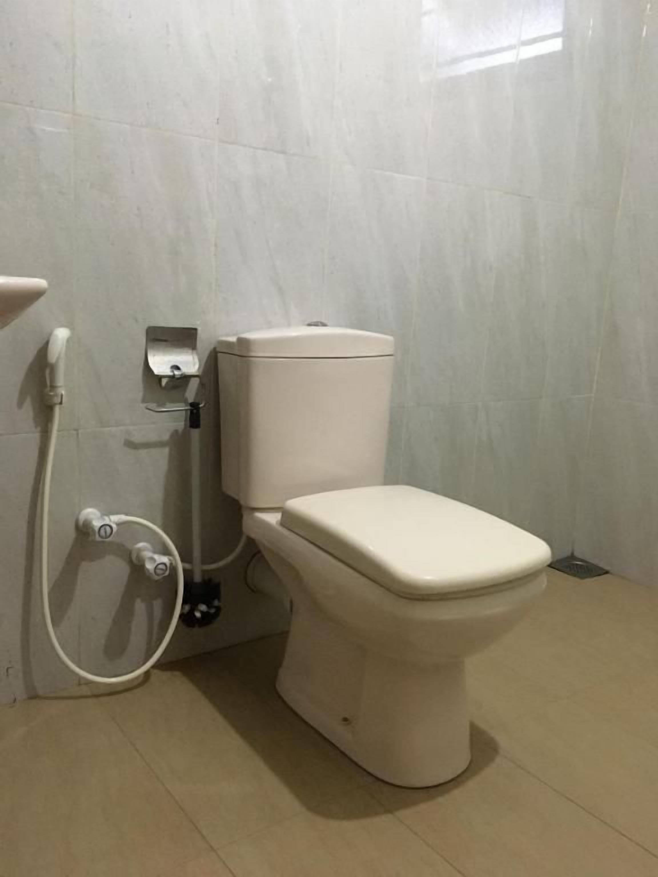 A standard toilet with a tank, a bidet attachment, and a wall-mounted flush handle.