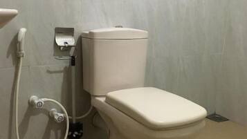 A standard toilet with a tank, a bidet attachment, and a wall-mounted flush handle.