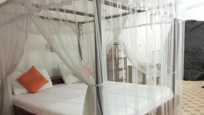 Una cama con dosel blanco y una almohada naranja.