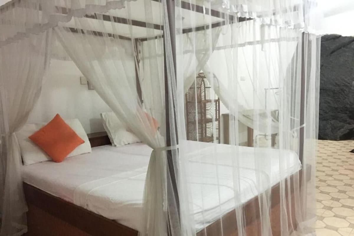 Una cama con dosel blanco y una almohada naranja.