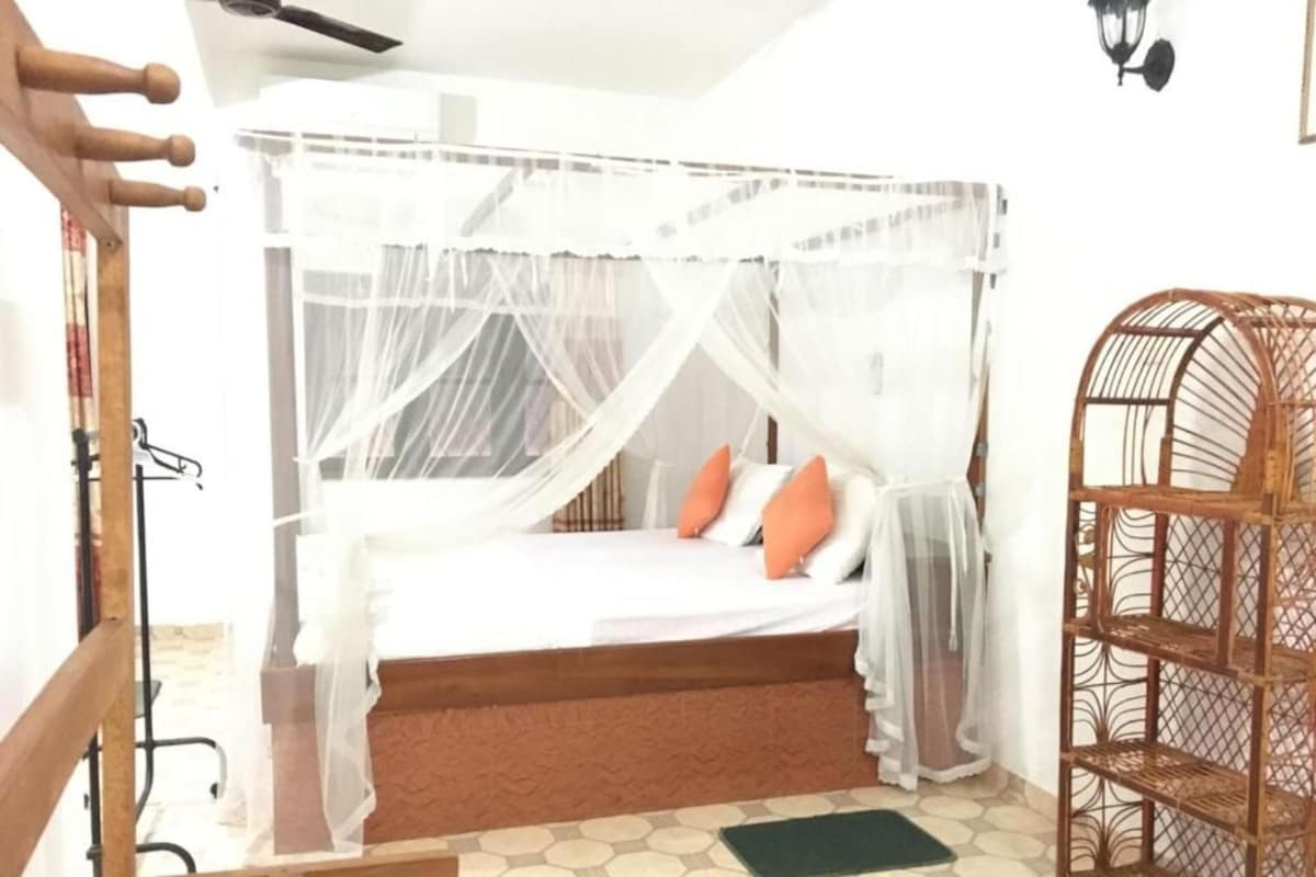 A bed with a canopy, a rattan chair, and a patterned floor.