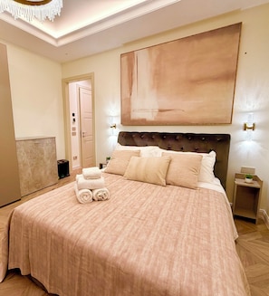 Habitación de hotel con una cama grande, cabecero, un cuadro en la pared y una mesita de noche con lámpara.
