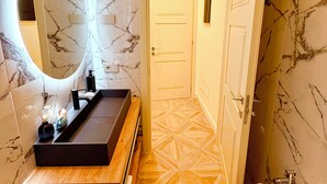 Ein Badezimmer mit Marmorwand, Waschtisch aus Holz, rundem Spiegel und Toilette.