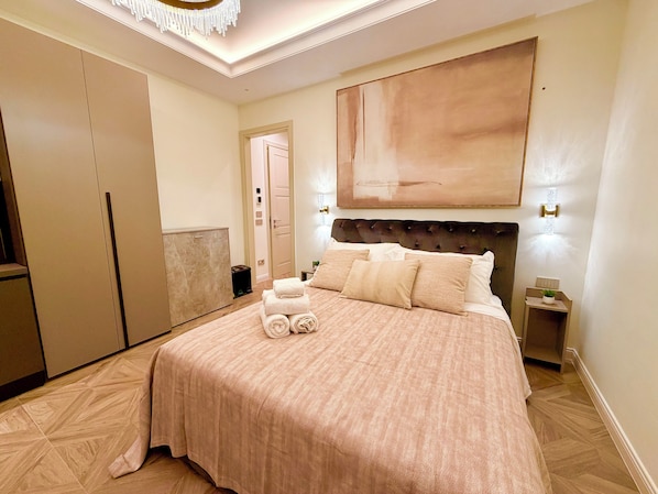 Habitación de hotel con una cama grande, un cabecero, un cuadro en la pared y una mesita de noche con una planta.