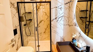 Ein modernes Badezimmer mit Marmorwand, Duschkabine, Toilette und Waschtisch inklusive Spiegel.
