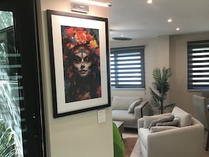 A framed artwork on a wall, a sofa, a potted plant, and a window with blinds. - LOL-HA House, by the sea—a secluded and peaceful spot (Isla Mujeres)
