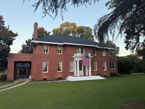 A two-story brick building with a front porch, a flag, and a well-maintained lawn. - 2 Bedrm Estate Phenix city. Minutes from uptown Columbus. More bedrooms soon! (Phenix City)