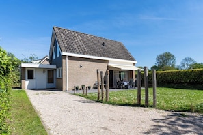 A two-story house with a gravel driveway, a covered patio area with outdoor seating, and a well-maintained lawn.