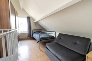 A dormitory room with a bunk bed, a sofa, a window with curtains, and a white railing.