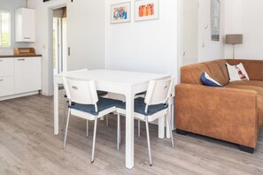 Um espaço de estar moderno com uma mesa de jantar branca e cadeiras, um sofá marrom e obras de arte na parede.