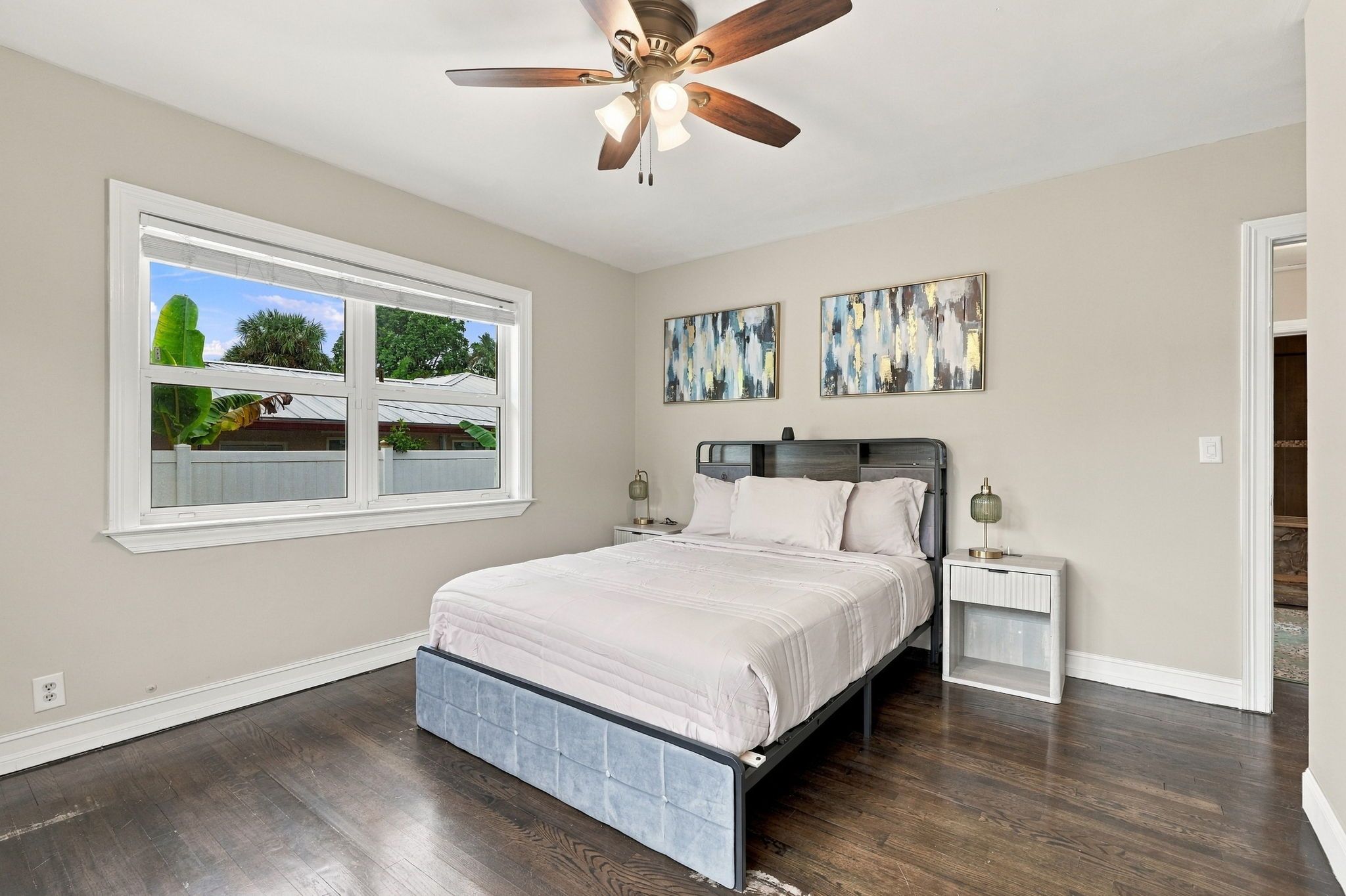 Un dormitorio con cama, ventilador de techo, ventana con vistas y dos lámparas de pared.