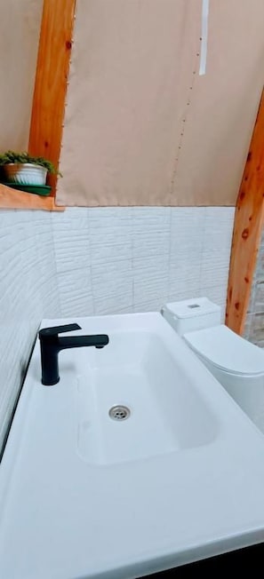 Un baño con lavabo blanco, grifo negro y retrete blanco.