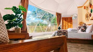 A tent-style room with a bed, a wooden desk, a plant, and a view of the outdoors.