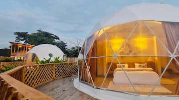 Ein kuppelförmiges Zelt mit Bett und Vorhängen, verbunden mit einer Holzterrasse.