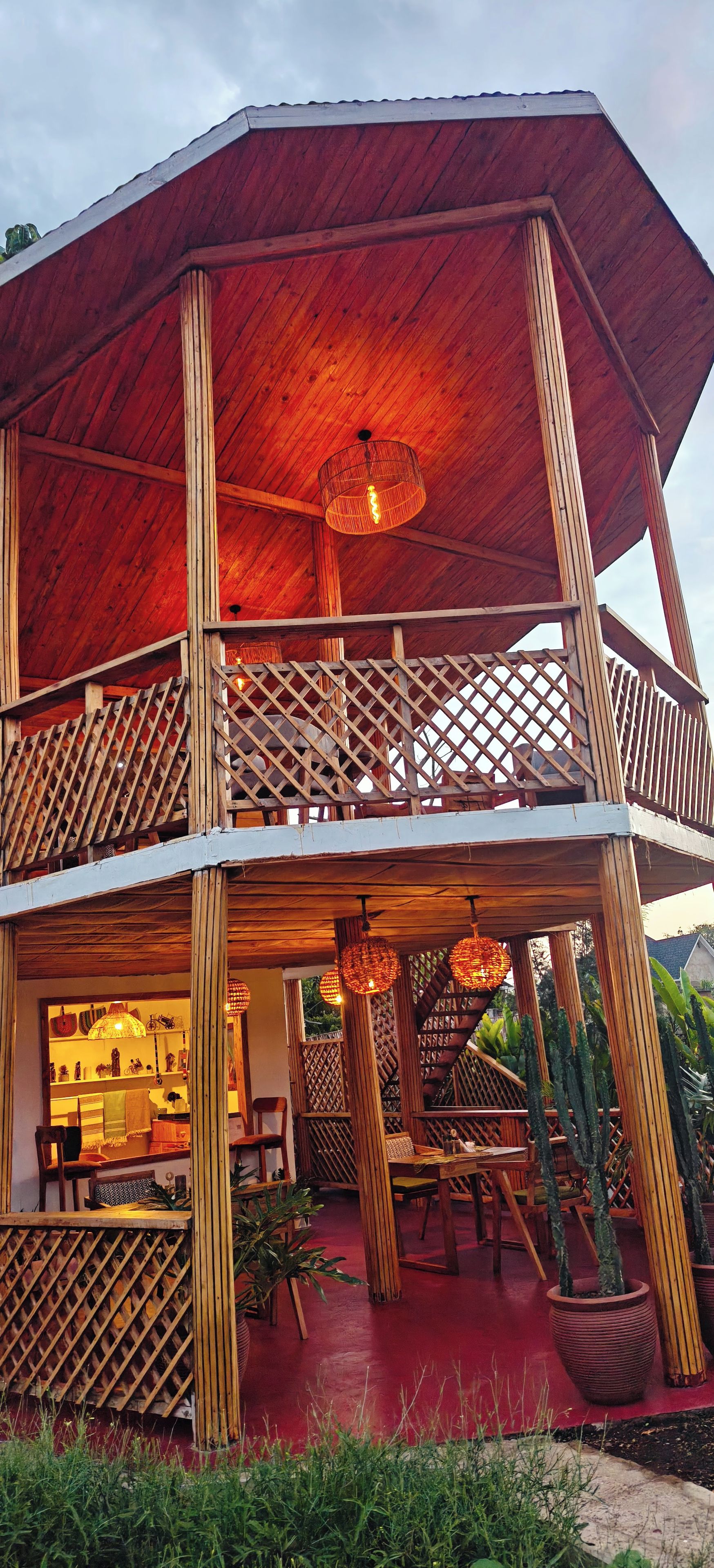 A two-story wooden structure with a balcony, potted plants, and a red floor.