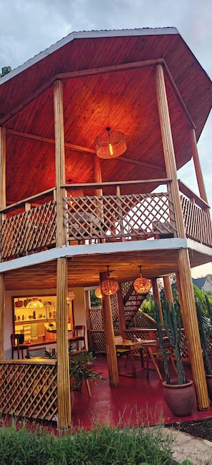 Une construction en bois à deux étages, dotée d’un balcon, de plantes en pot et d’un plancher rouge.