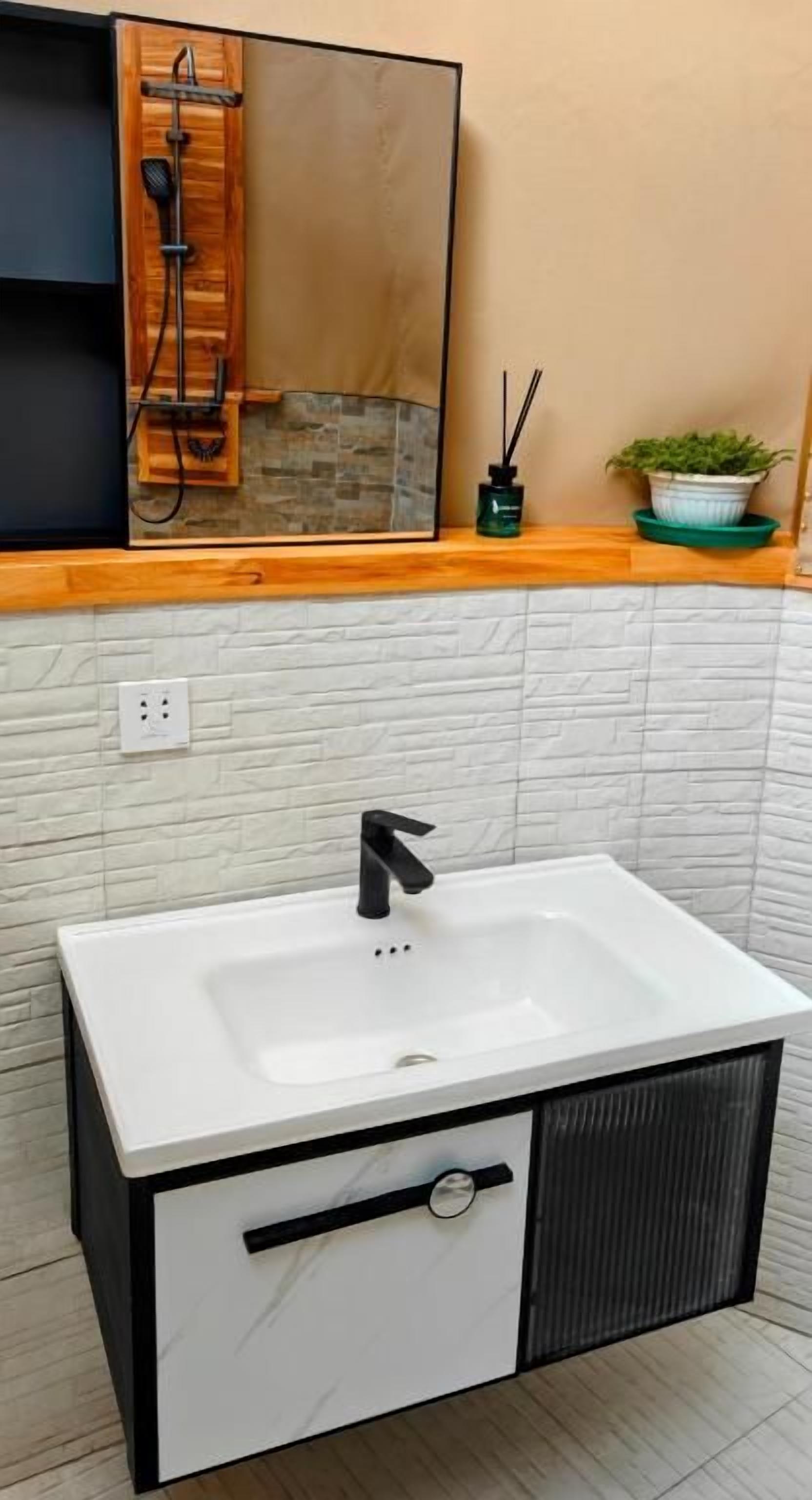 A bathroom with a white sink, black faucet, and a wooden shelf above.