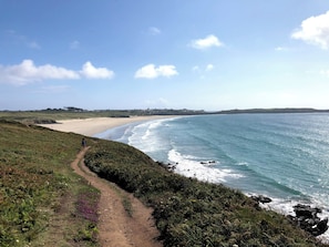 Un sentier côtier qui mène à une plage d’où l’on a une vue dégagée sur l’océan et les collines lointaines.
