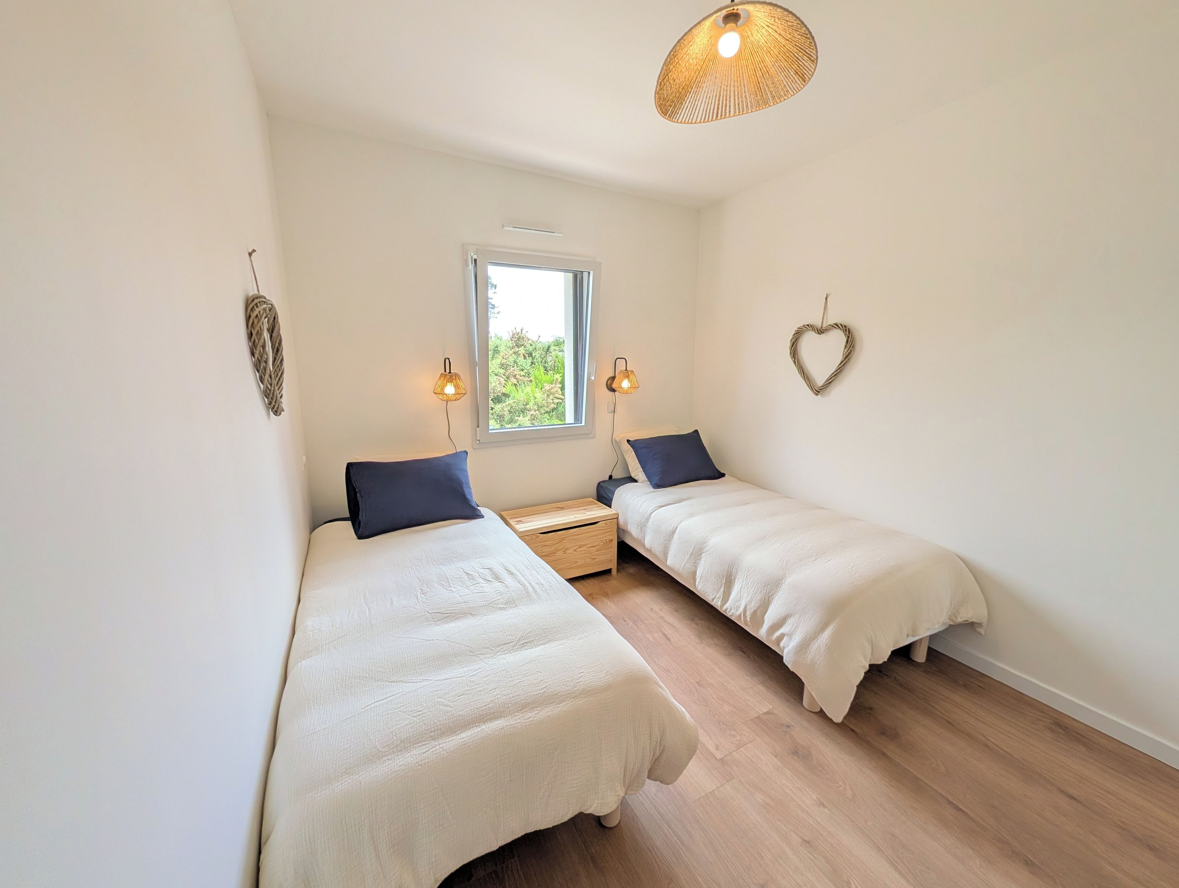 Una camera da letto con due letti singoli, una finestra, un lampadario e una decorazione a forma di cuore sulla parete.