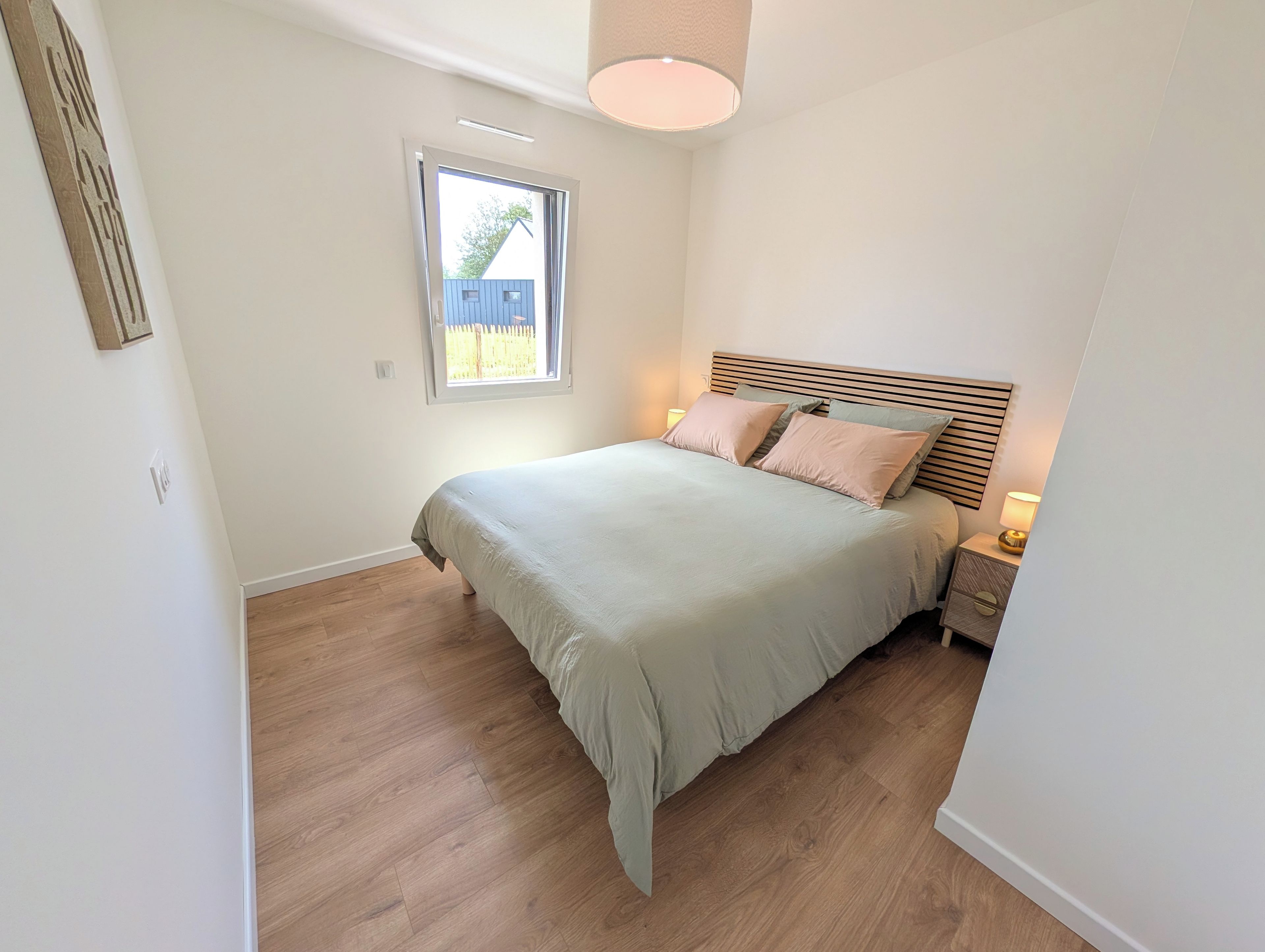 Une chambre à coucher avec un lit, un plancher en bois, une fenêtre et une lampe de chevet.