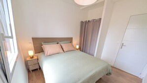 Ein Schlafzimmer mit einem Bett, Nachttischen, einem Fenster und einer Tür.