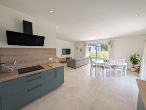 A modern kitchen with a built-in oven, a dining area with white chairs, and a large window overlooking a garden. - Vrbo Property (Le Conquet)