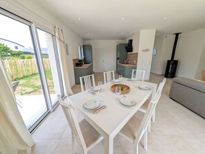 A modern dining area with a white table set for four, surrounded by chairs, with a kitchen in the background. - Vrbo Property (Le Conquet)