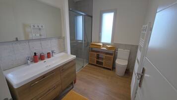 Une salle de bain avec un meuble-lavabo en bois, une cabine de douche en verre, des toilettes et une fenêtre qui laisse entrer la lumière naturelle.