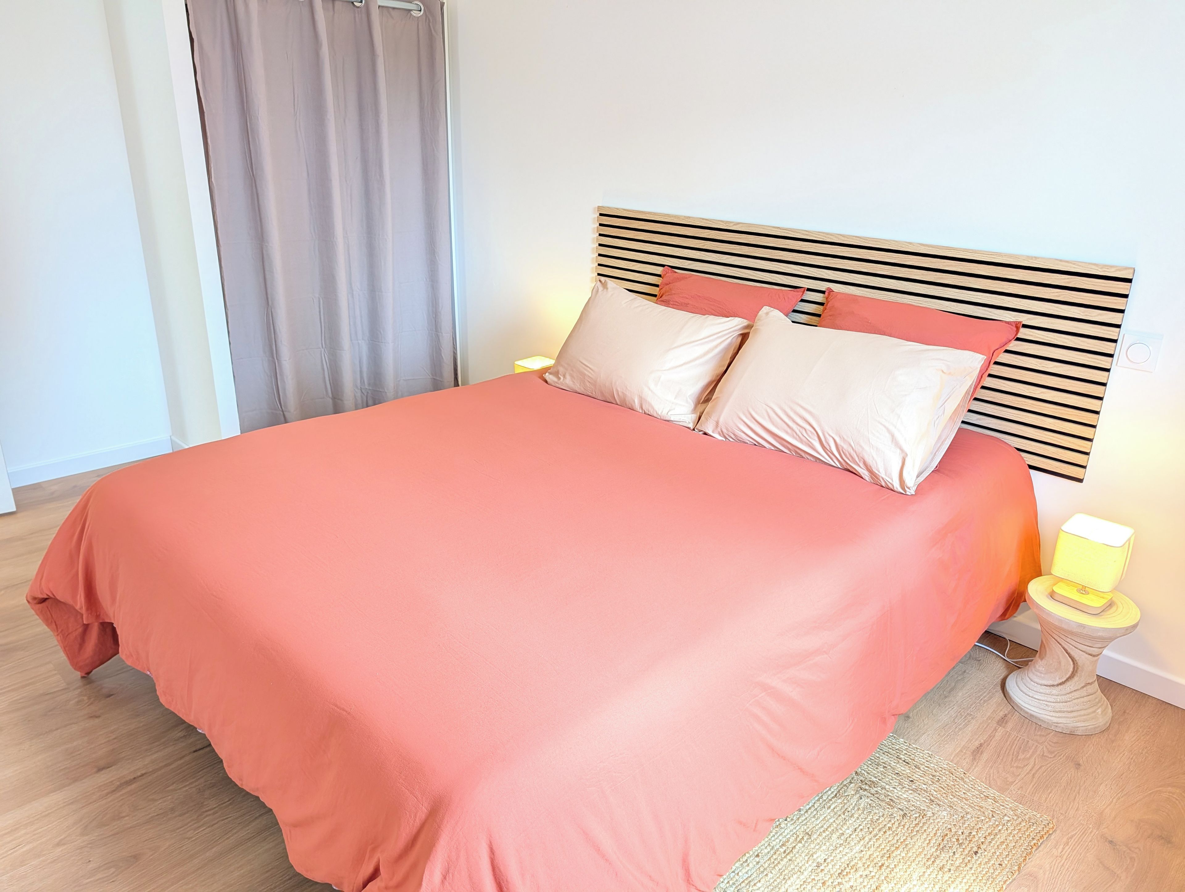 Una cama con cabecera de madera, colcha rosa y dos almohadas.