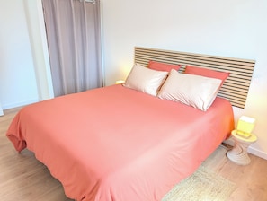 Una cama con cabecera de madera, colcha rosa y dos almohadas.