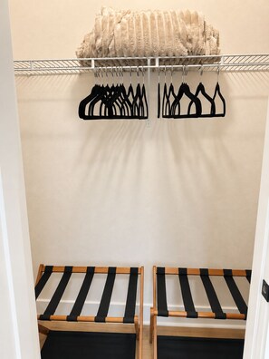 Une chambre comprenant un lit, un portant à vêtements avec des cintres et un meuble de rangement contenant des vêtements pliés.