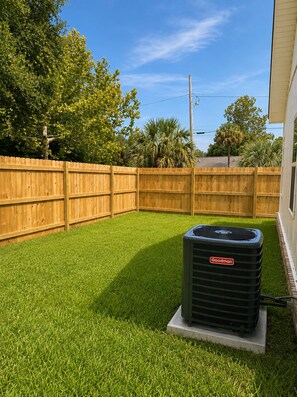 A backyard with a wooden fence, green artificial grass, and an air conditioning unit. - SunKissed on the Coast, well appointed, high-end home near DT. SMEG Espresso (Pensacola)