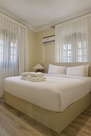 A hotel room with a large bed, white linens, a nightstand with a lamp, and a window with sheer curtains. - VESTA  - Luxury APT - 2BR - South Teseen (II) (New Cairo City)