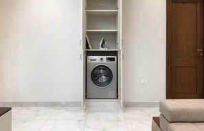 Uma lavanderia com máquina de lavar, secadora e prateleira com objetos.