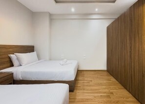 Hotellihuone, jossa on kaksi sänkyä, puiset päätylevyt, valkoiset vuodevaatteet ja puulattia.