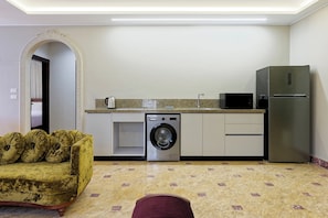 A compact living space with a washing machine, a microwave, and a refrigerator. - Luxury APT - 2BR - South Teseen (I) (New Cairo City)