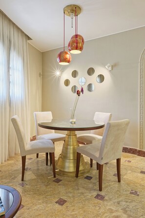 A dining area with a round table, white chairs, a gold base, and a chandelier with red and gold spherical lamps. - Luxury APT - 2BR - South Teseen (I) (New Cairo City)