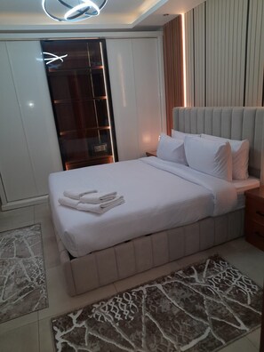 A modern bedroom with a large bed, a bedside table, a wardrobe, and a built-in bench.