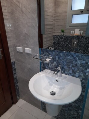Un baño con lavamanos blanco, un espejo encima y una zona de ducha con puerta de cristal.