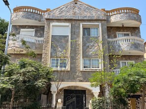 A multi-story building with a stone facade, balconies, and a central entrance with a decorative door. - VESTA  - Luxury APT - 3BR - New Cairo (XXX) (New Cairo City)