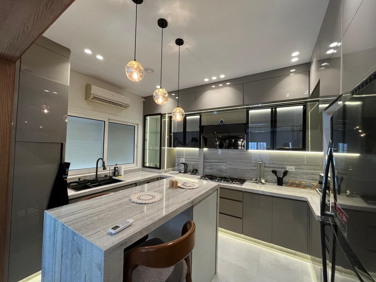 A modern kitchen with a marble countertop, stainless steel appliances, pendant lighting, and a central island.