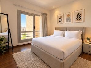 A hotel room with a large bed, a window with curtains, a bedside table with a lamp, and a plant. - VESTA - Luxury Apt- 3br - cfc (xlvii) (New Cairo City)
