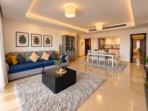 Ein modernes Wohnzimmer mit Sofa, Couchtisch und Essbereich. An der Wand hängen gerahmte Bilder, ein Schrank und im Hintergrund eine Küche.