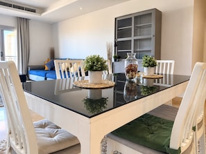 A dining area with a glass table, white chairs, a blue sofa, and a cabinet in the background. - VESTA - Luxury Apt- 3br - cfc (xlvii) (New Cairo City)