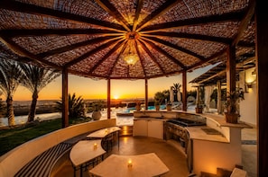 Ein überdachter Außenbereich mit Pool, Sitzgelegenheiten und Blick auf den Sonnenuntergang.