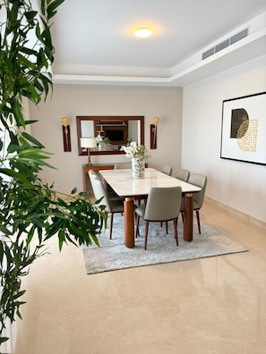A dining area with a marble table, chairs, a vase with flowers, a wall-mounted mirror, and a framed picture. - VESTA - Luxury Apt- 3br - cfc (xlviii) (New Cairo City)