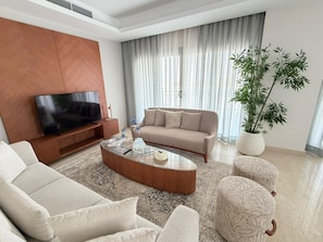 A modern living room with a flat-screen TV, a beige sofa, a round coffee table, and a large potted plant. - VESTA - Luxury Apt- 3br - cfc (xlix) (New Cairo City)