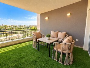 A balcony with artificial grass, wicker furniture, and a view of buildings. - VESTA Luxury APT - 2Br - cfc (xc) (New Cairo City)