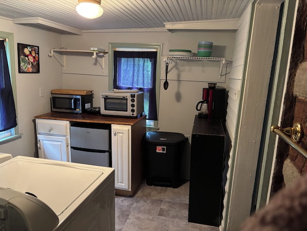 A compact kitchenette with a microwave, toaster oven, and a coffee maker on a shelf.