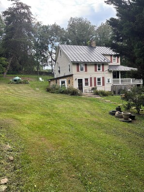 Ein zweistöckiges Haus mit Stein Fundament, einer Veranda und einem umzäunten Garten.